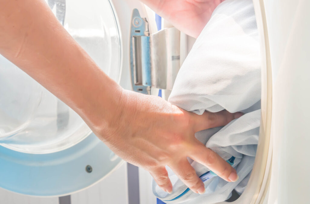 Closeup of woman 's hand. Putting dirty clothes in laundry bags into washing machine, to avoid releasing garment microfibers into the environment, Impact of Microfibers on the Environment