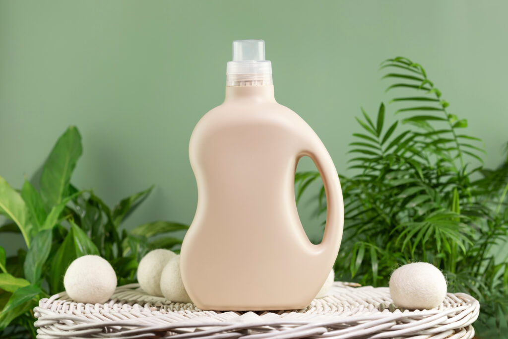 Natural laundry detergent mockup. Washing detergent concept with bottles of washing gel or fabric softener on a white laundry basket on a green background with green leaves, eco-friendly detergent, sustainable stain removal